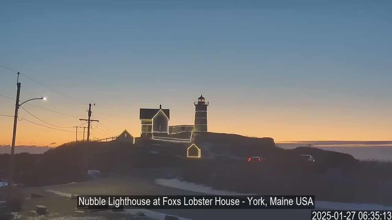A lighthouse and adjacent buildings are illuminated at sunset on a clear evening.