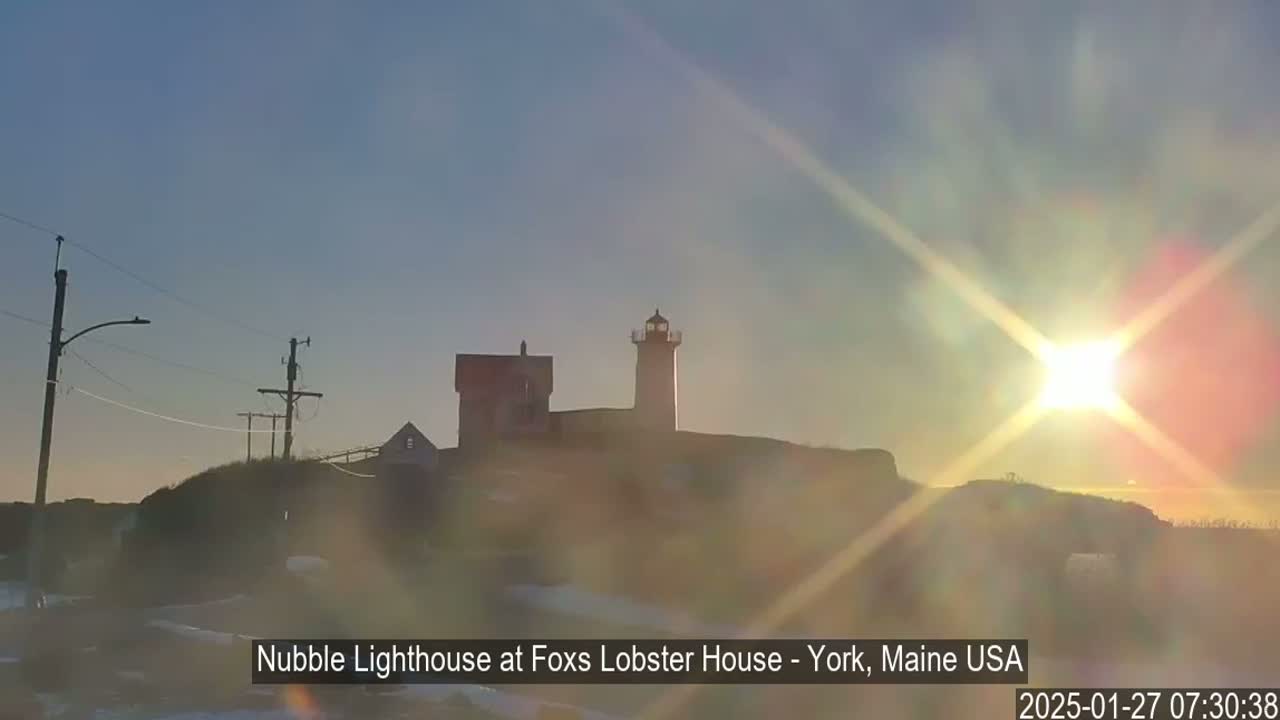 A lighthouse and other buildings are silhouetted against a bright, sunrise sky.