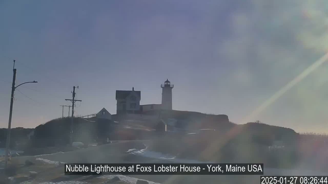 A lighthouse and adjacent buildings sit atop a hazy hill on a sunny, but slightly overcast day.