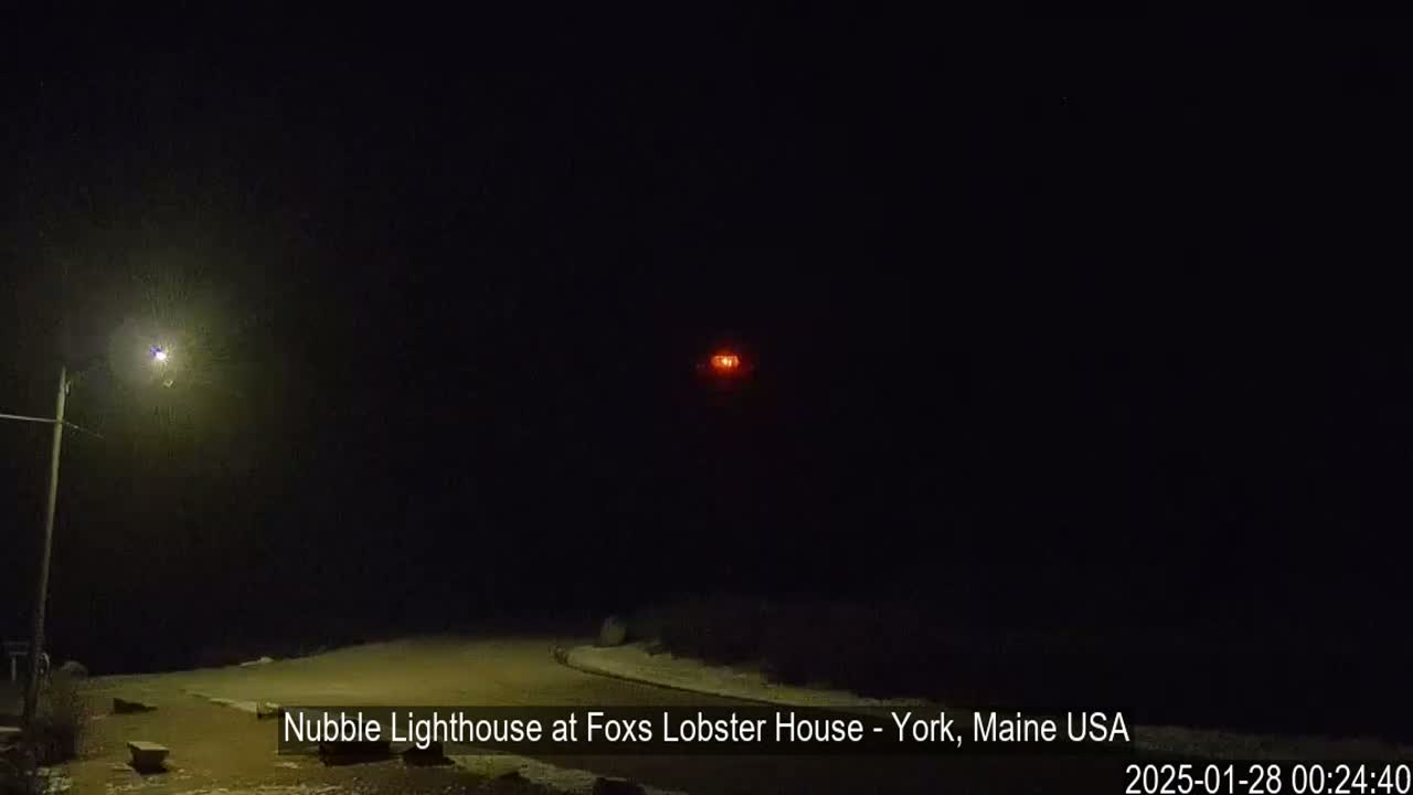 A nighttime scene shows a lit lighthouse in the distance, a streetlight to the left, and a snow-covered ground.