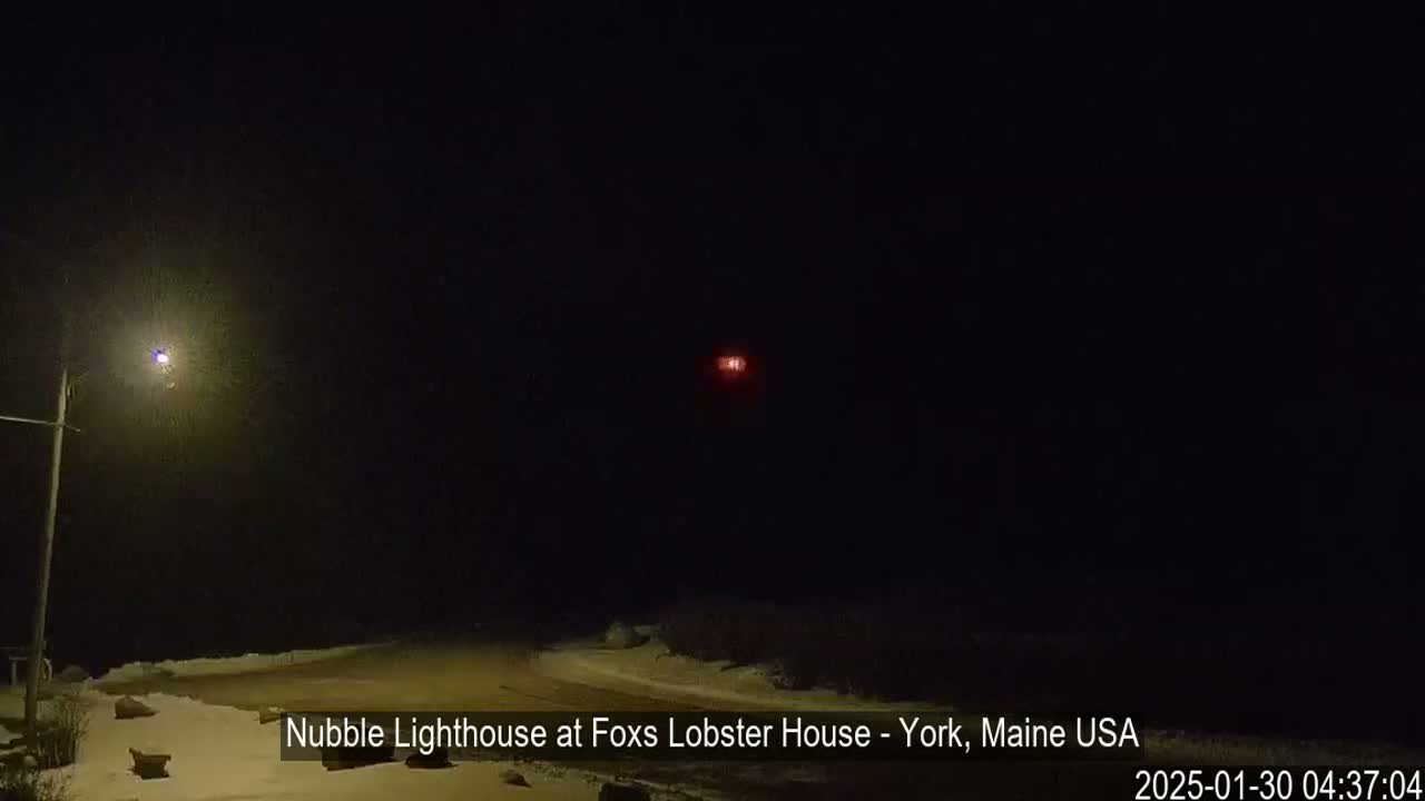 A dimly lit snow-covered scene at night shows a lighthouse in the distance.