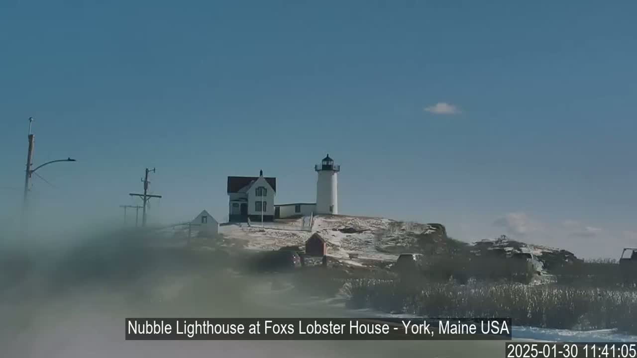 A lighthouse and adjacent building are situated on a snow-covered hill under a clear blue sky.