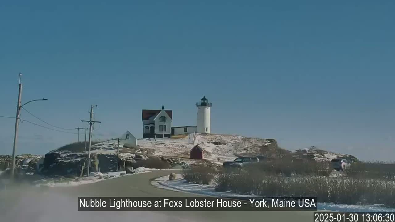 A white lighthouse and keeper's house sit atop a snow-dusted hill on a clear, sunny day.