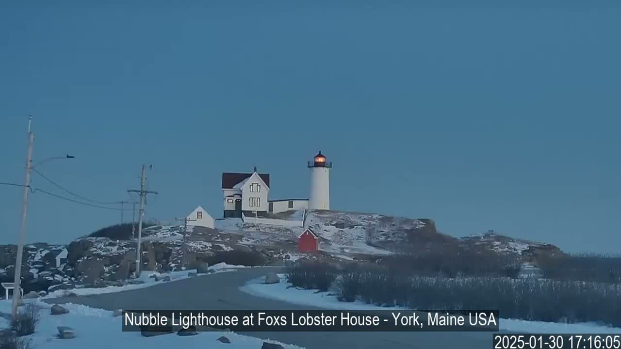 A lighthouse and keeper's house sit atop a snow-covered rocky outcrop under a clear twilight sky.