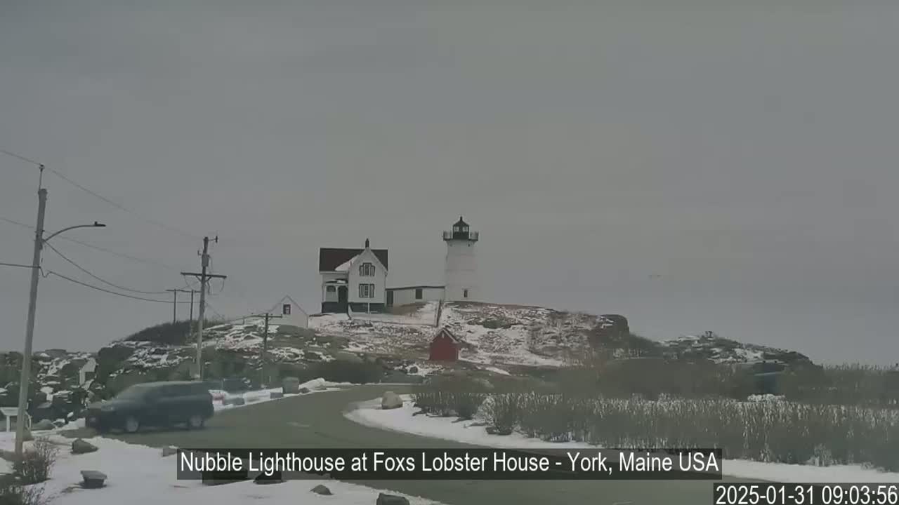 A lighthouse and a house sit atop a snow-covered rocky hill on an overcast day.