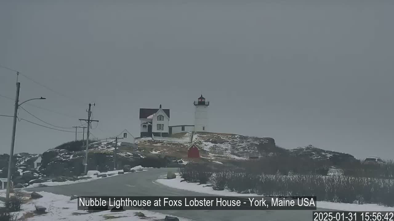 A lighthouse and a house sit atop a snow-dusted rocky hill on an overcast day.