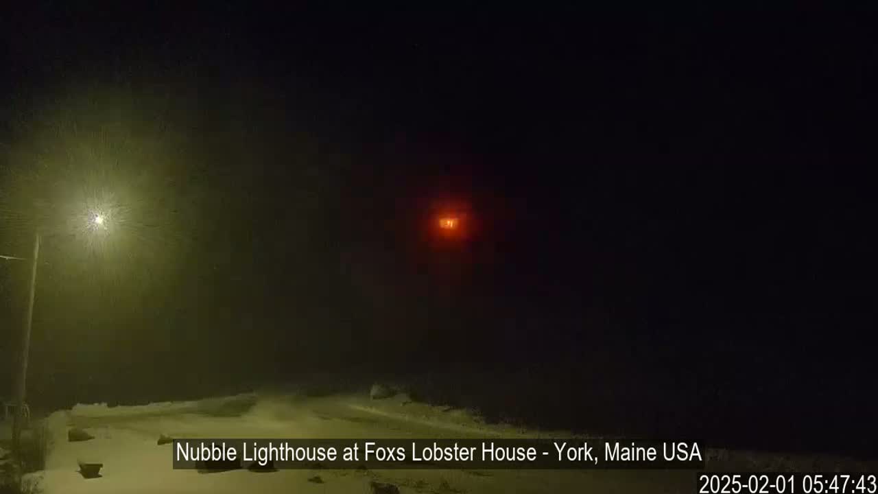 A dimly lit snowy scene at night shows a lighthouse in the distance, illuminated by its own light.