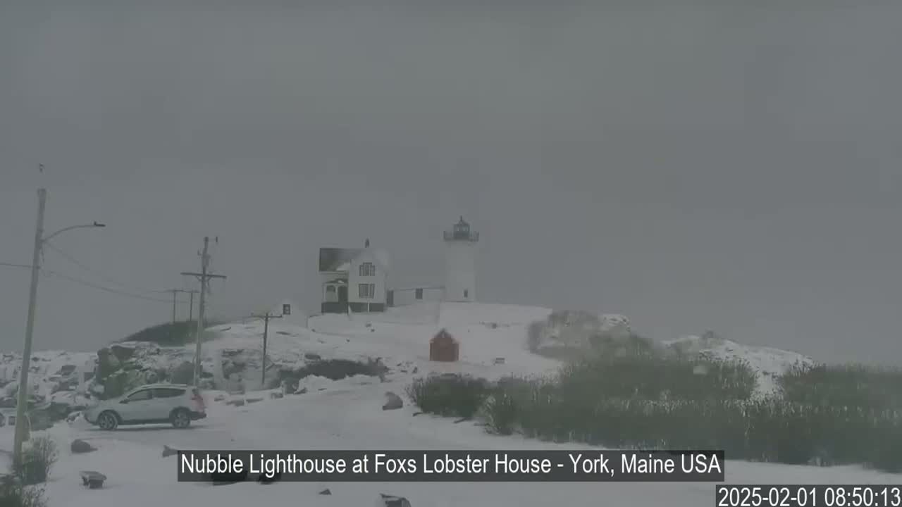 A lighthouse and a house are covered in snow under a heavily overcast sky.