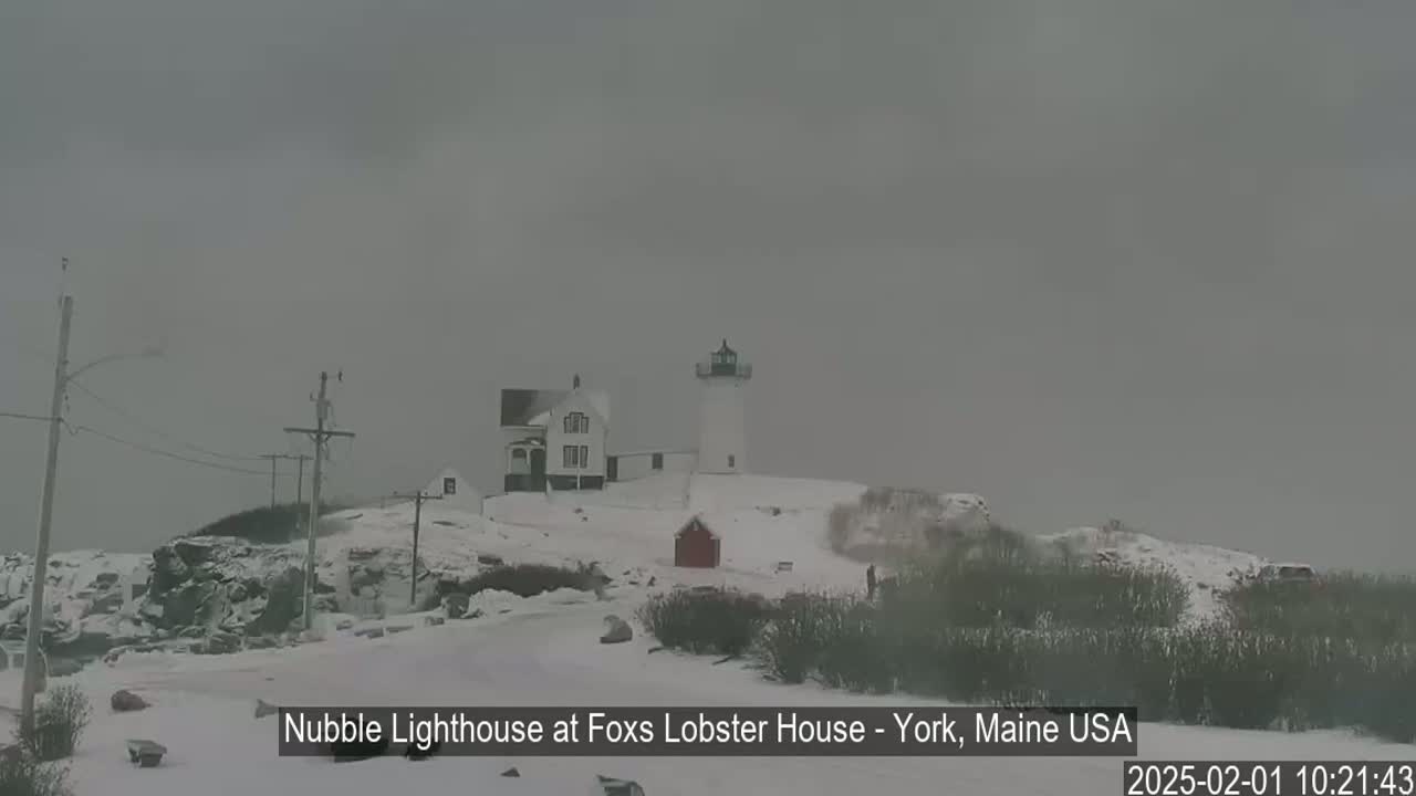 A snow-covered lighthouse and nearby building are visible in an overcast, snowy scene.