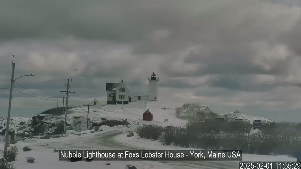 A snow-covered lighthouse and accompanying building are visible under a cloudy sky.