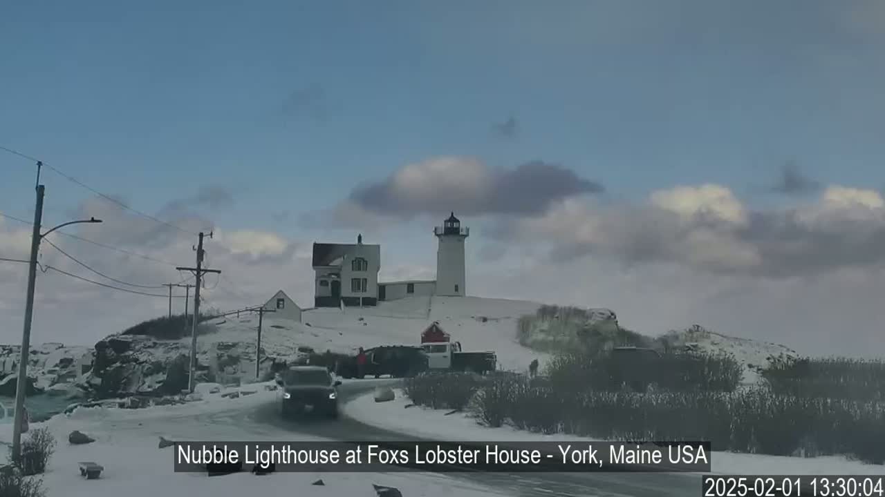 A snow-covered lighthouse and adjacent buildings are visible on a partially cloudy day.