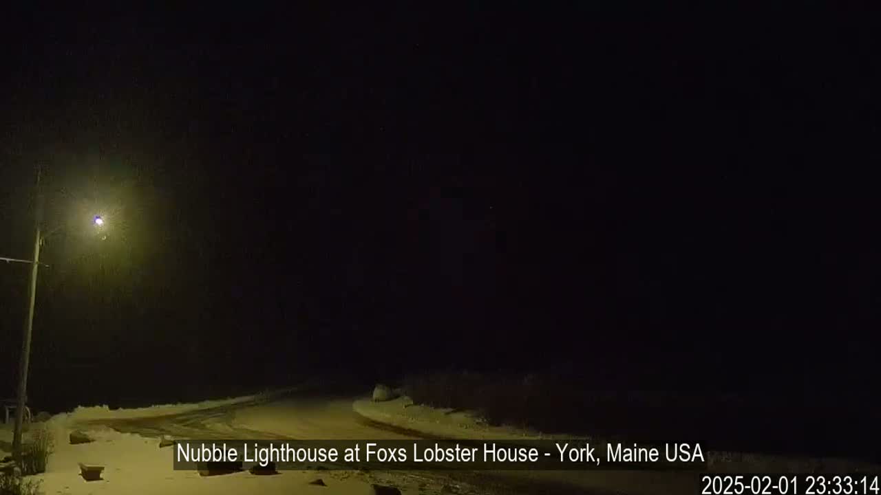 A snow-covered road at night is illuminated by a single streetlight.