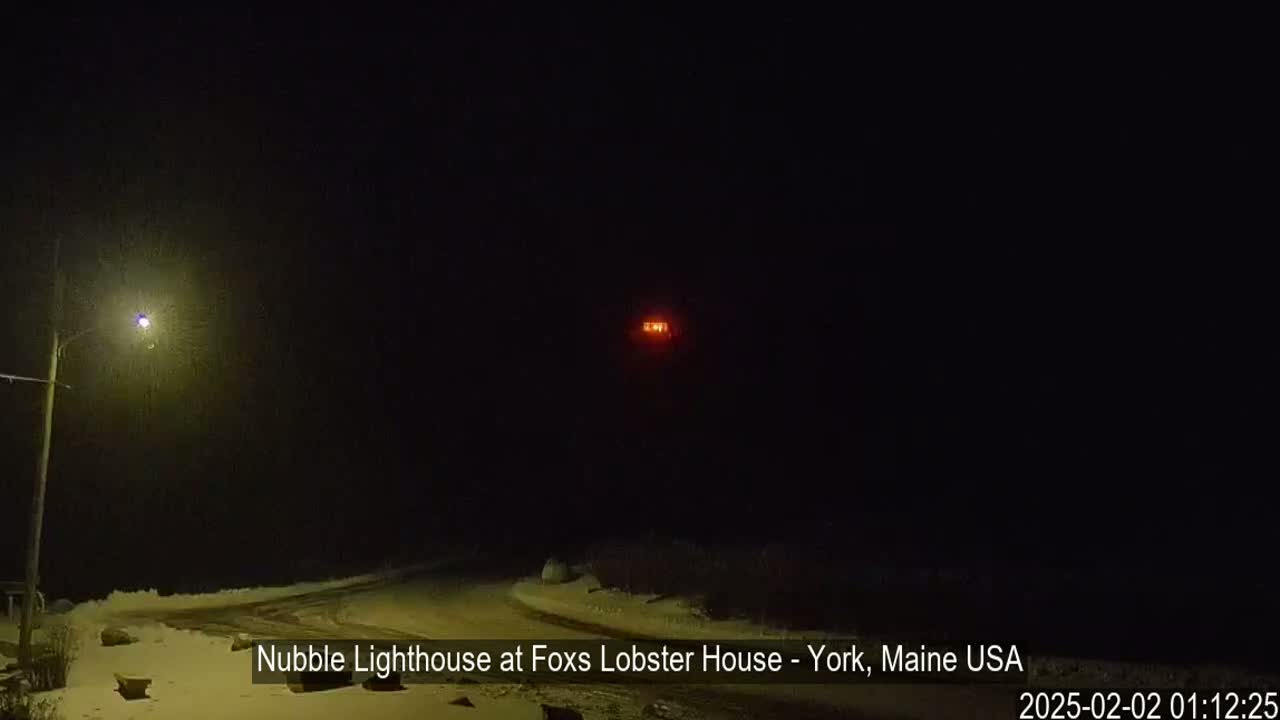 A distant, lit lighthouse is visible in the dark, snowy nighttime.