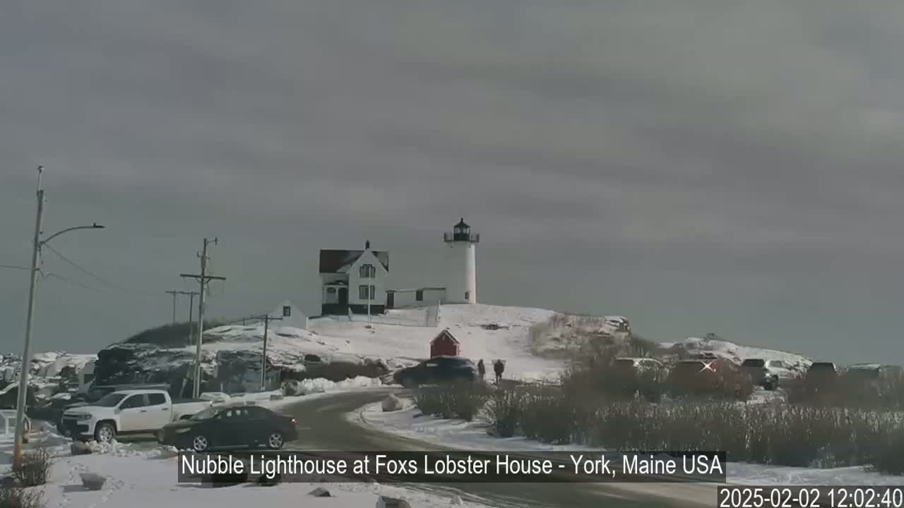 A snow-covered lighthouse and accompanying buildings are visible from a roadside vantage point under an overcast sky.