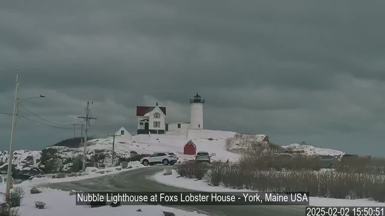 A lighthouse and a house sit on a snow-covered hill under an overcast sky.
