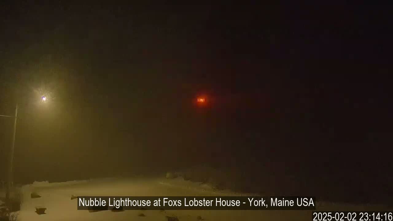 A dimly lit snowy scene at night, shrouded in fog, with a distant red light visible.