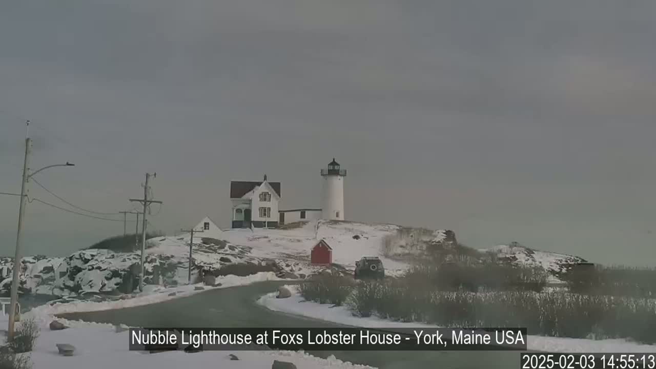 A snow-covered landscape features a lighthouse and a white building on a rocky hill under an overcast sky.