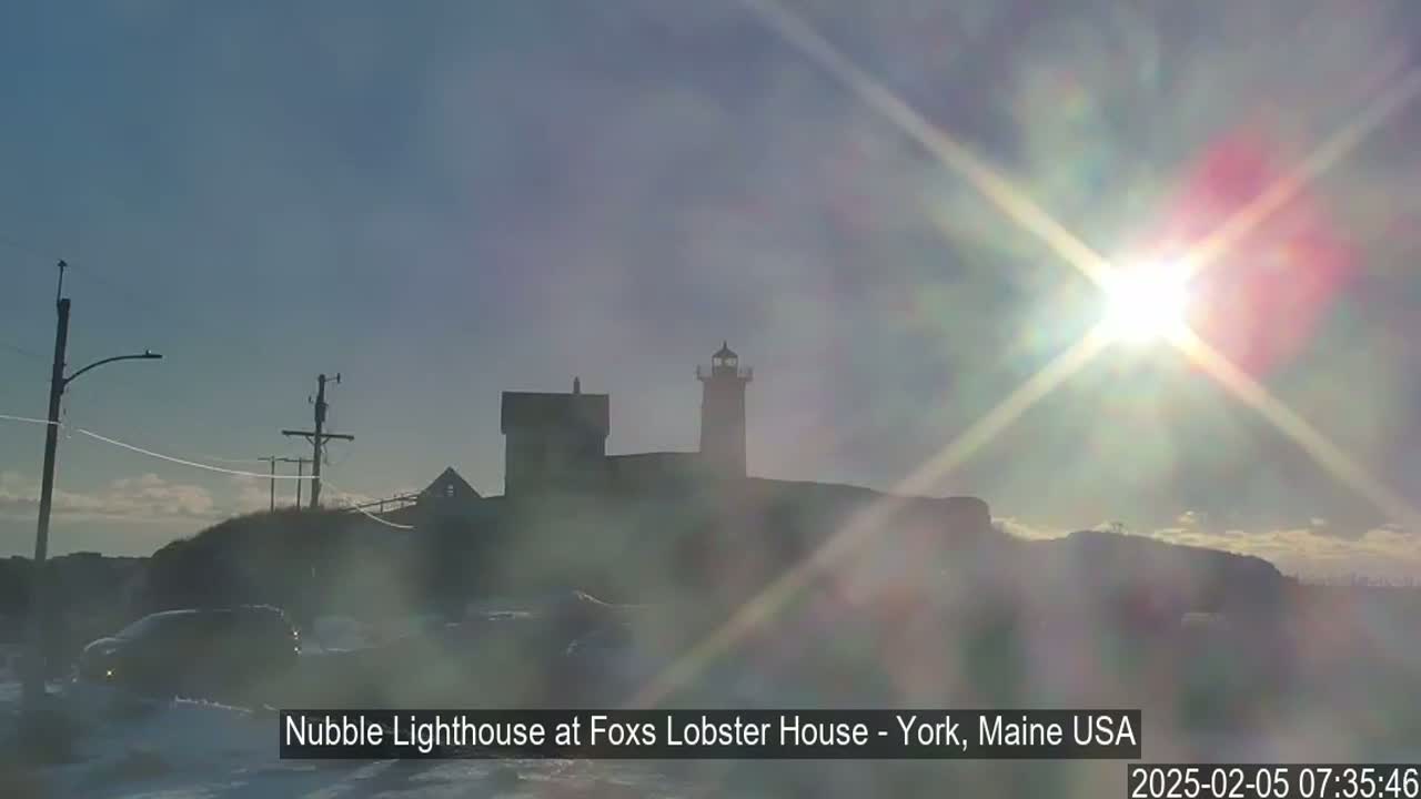 A lighthouse sits on a snow-covered hill under a bright, sunny sky.