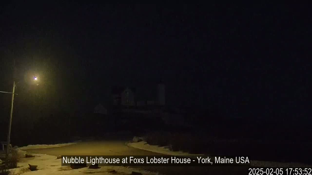 A dimly lit lighthouse is visible in the distance on a dark, snowy night.