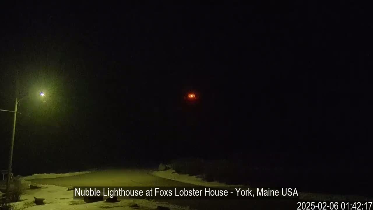A nighttime view of a snow-covered landscape with a lit streetlight and a distant, glowing red light.