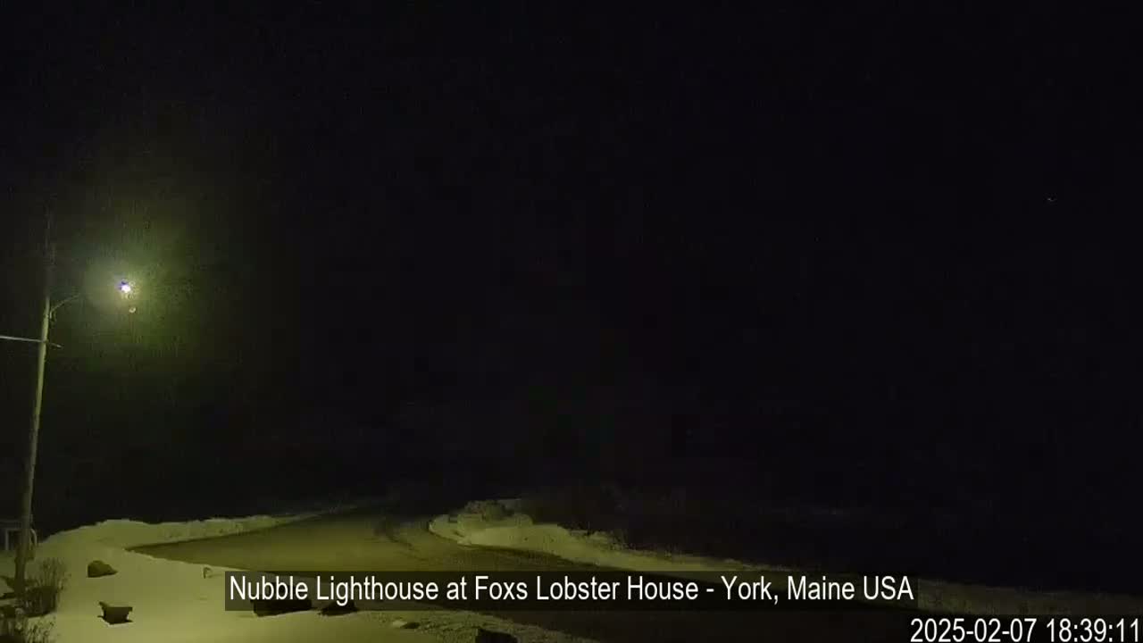 A nighttime, snow-covered coastal scene is illuminated by a single lamppost.