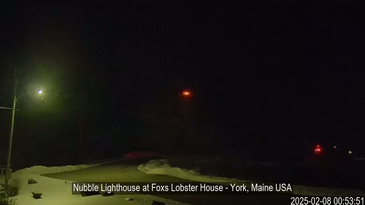 A nighttime view of a lighthouse with some snow on the ground.