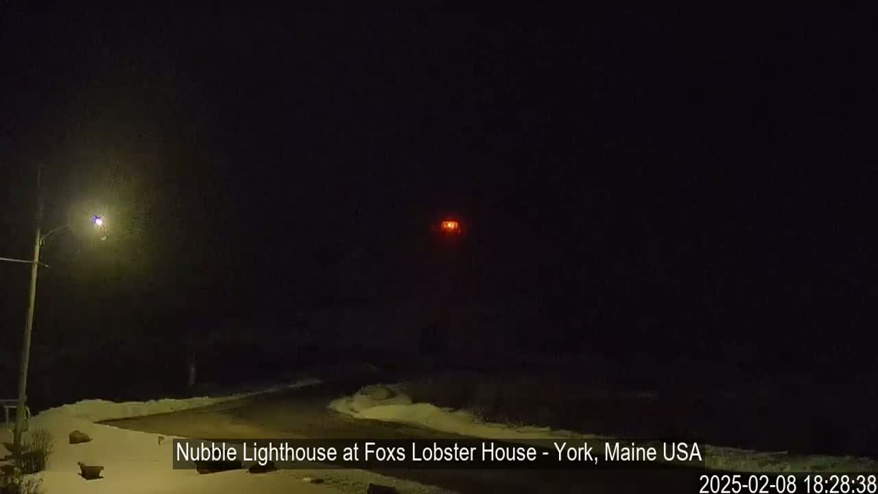 A nighttime, snowy scene shows a distant, faintly glowing lighthouse under a dark sky.