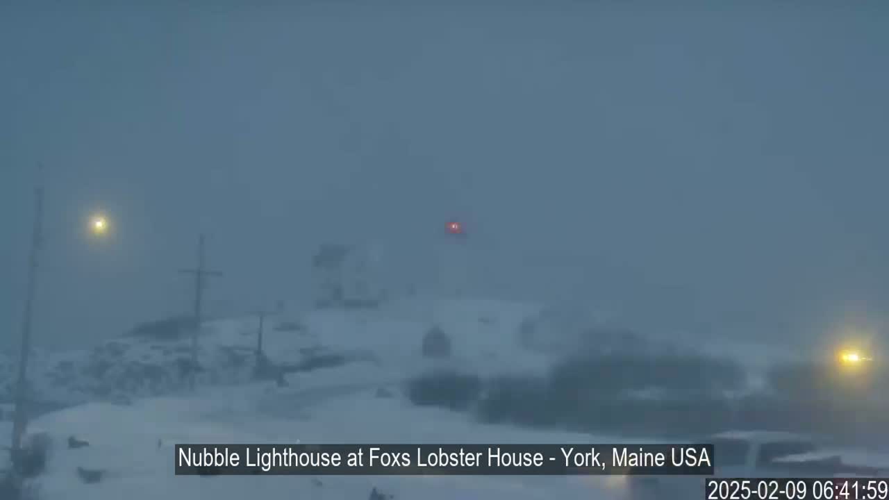 A snowstorm obscures a view of a lighthouse and surrounding snowy landscape.