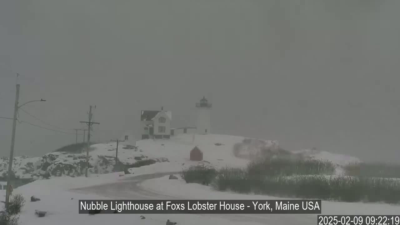 A lighthouse and accompanying buildings are covered in snow during a heavy snowstorm.