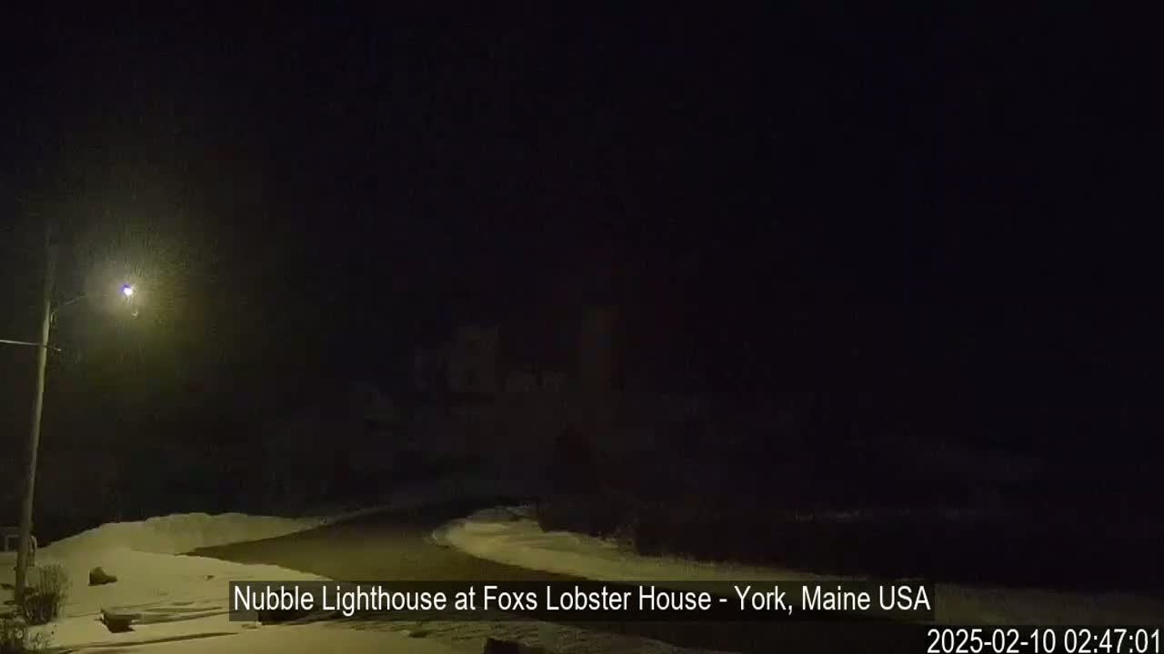 A dark, snow-covered road curves gently into a dimly lit nighttime scene.