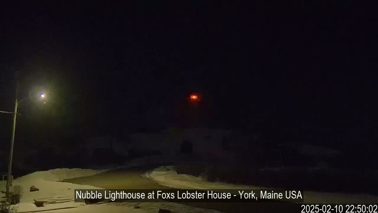 A nighttime view of a lighthouse with a red light atop a snow-covered landscape under a dark sky.