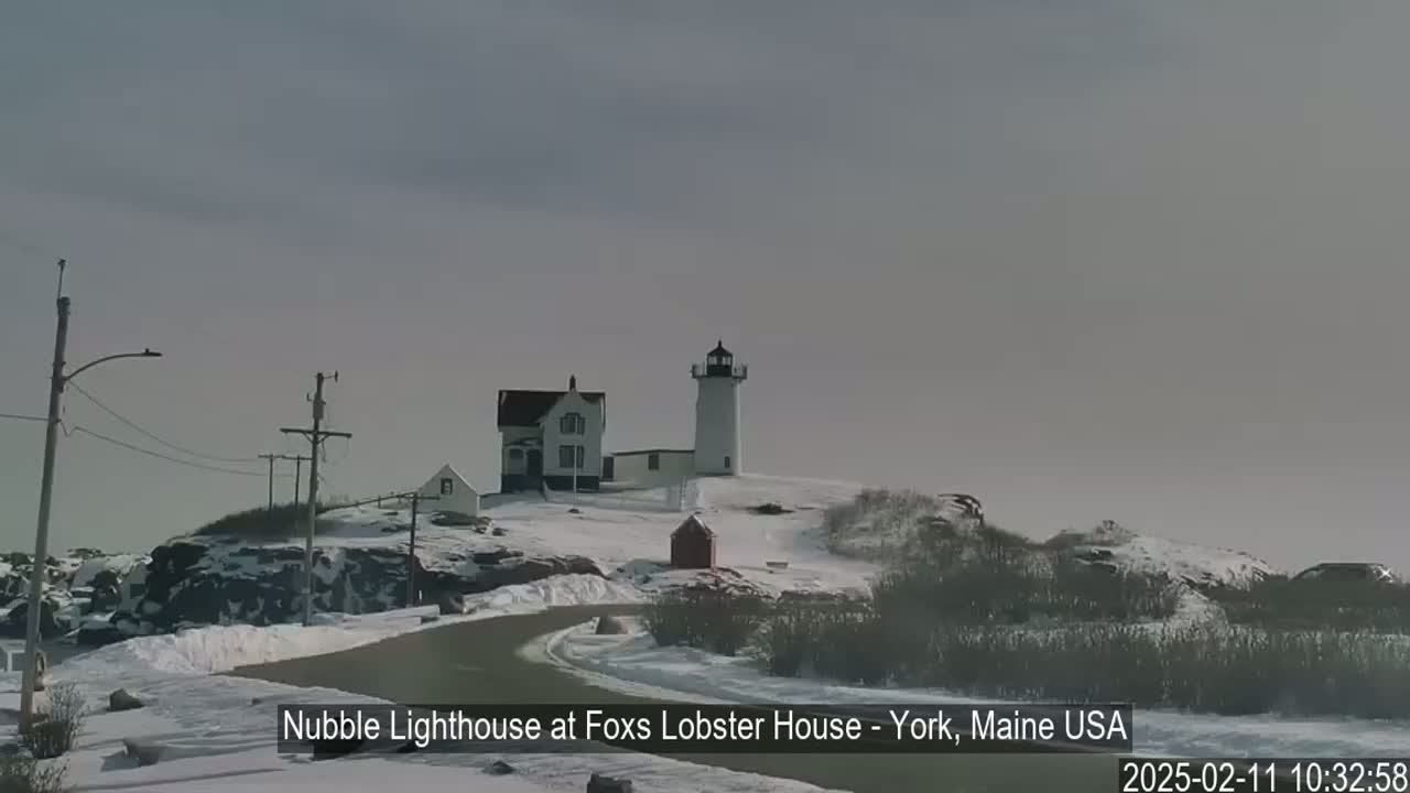 A lighthouse and adjacent buildings sit atop a snow-covered hill on a cloudy day.