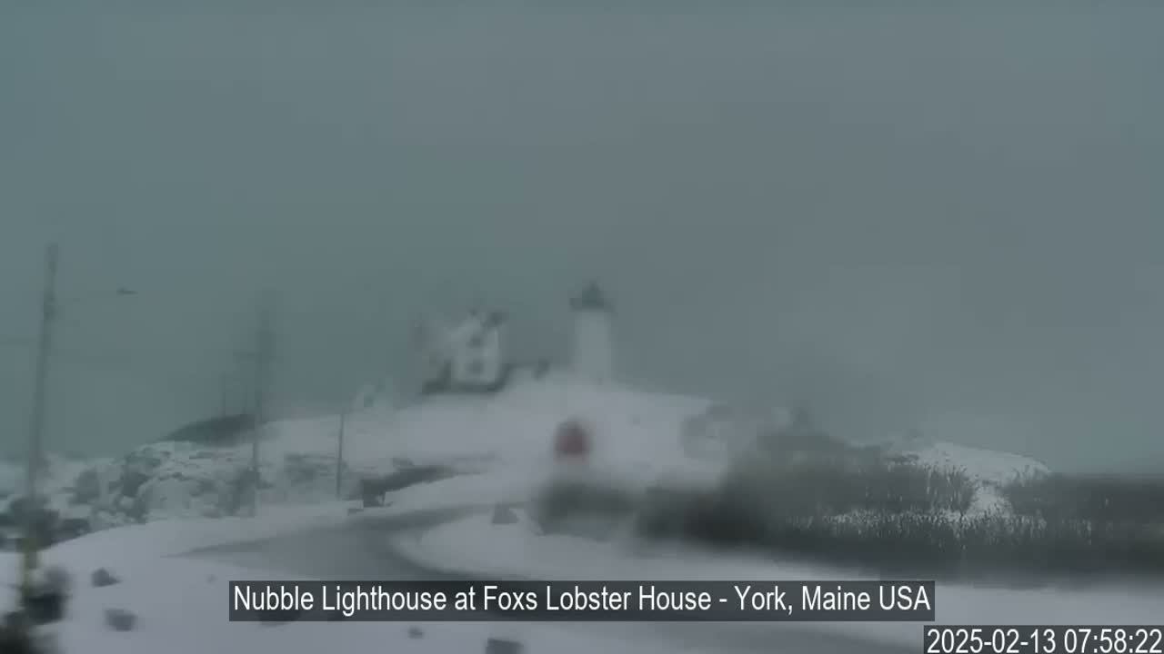 A lighthouse is barely visible through heavy snow and fog.