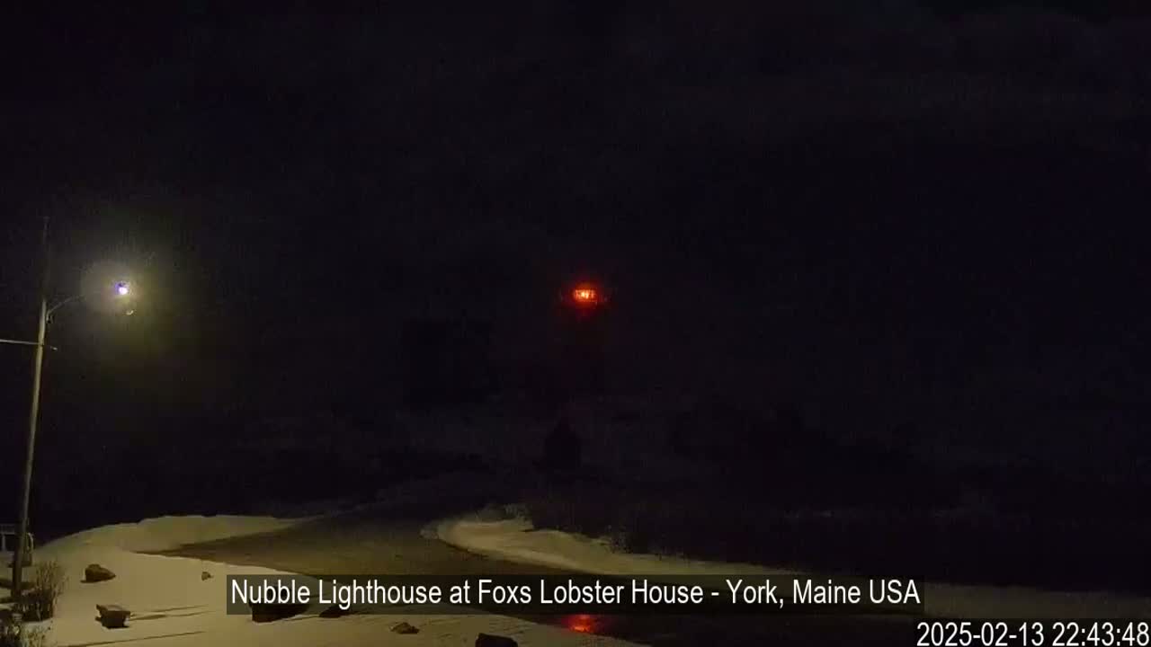 A red light from a lighthouse is visible in the distance on a dark, snowy night.