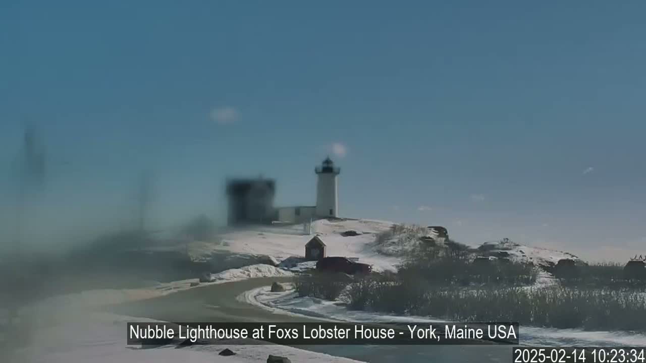 A white lighthouse sits atop a snow-covered hill on a clear, sunny day.