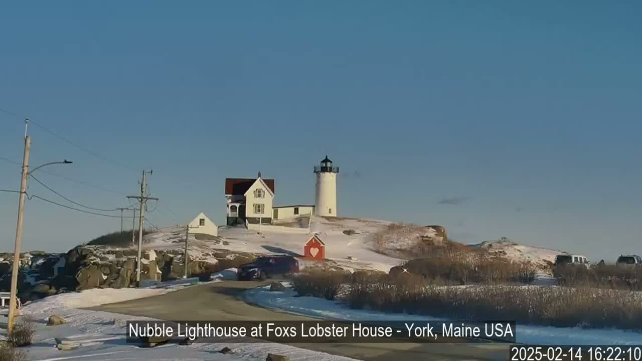 A lighthouse and other buildings sit on a snow-covered hill on a clear, sunny day.