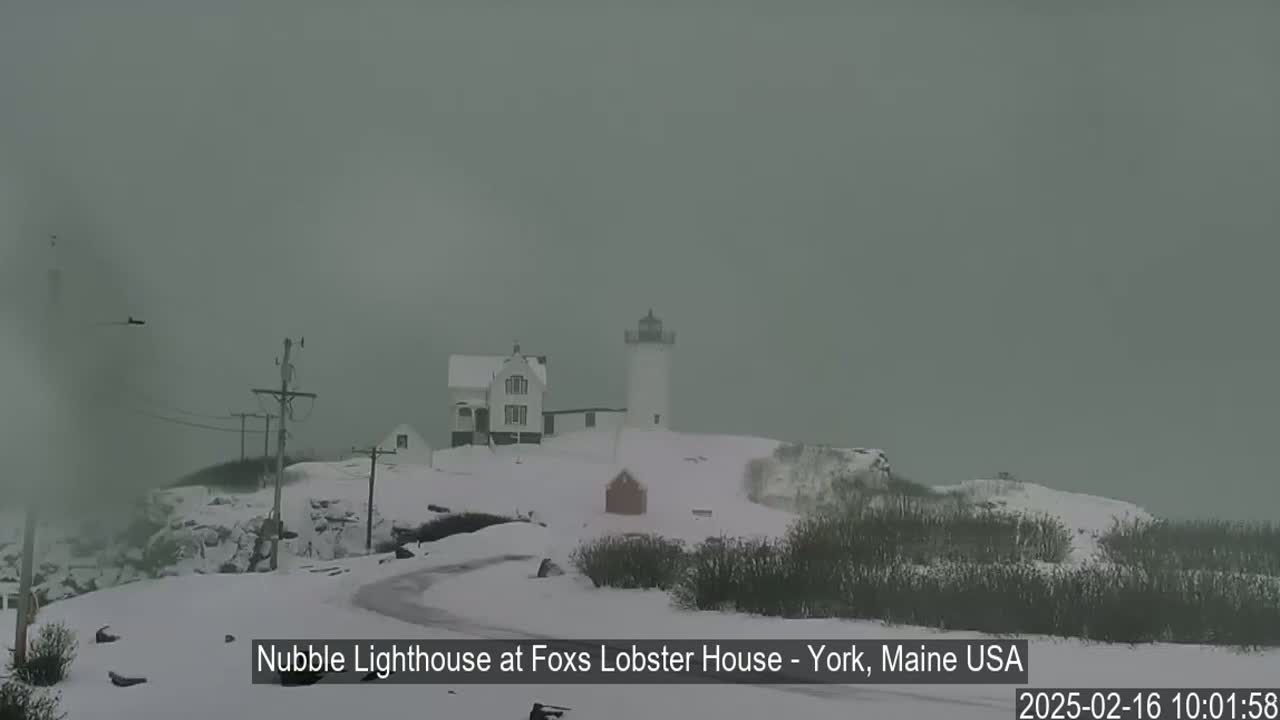 A snow-covered lighthouse and nearby buildings are visible in a hazy, overcast winter scene.