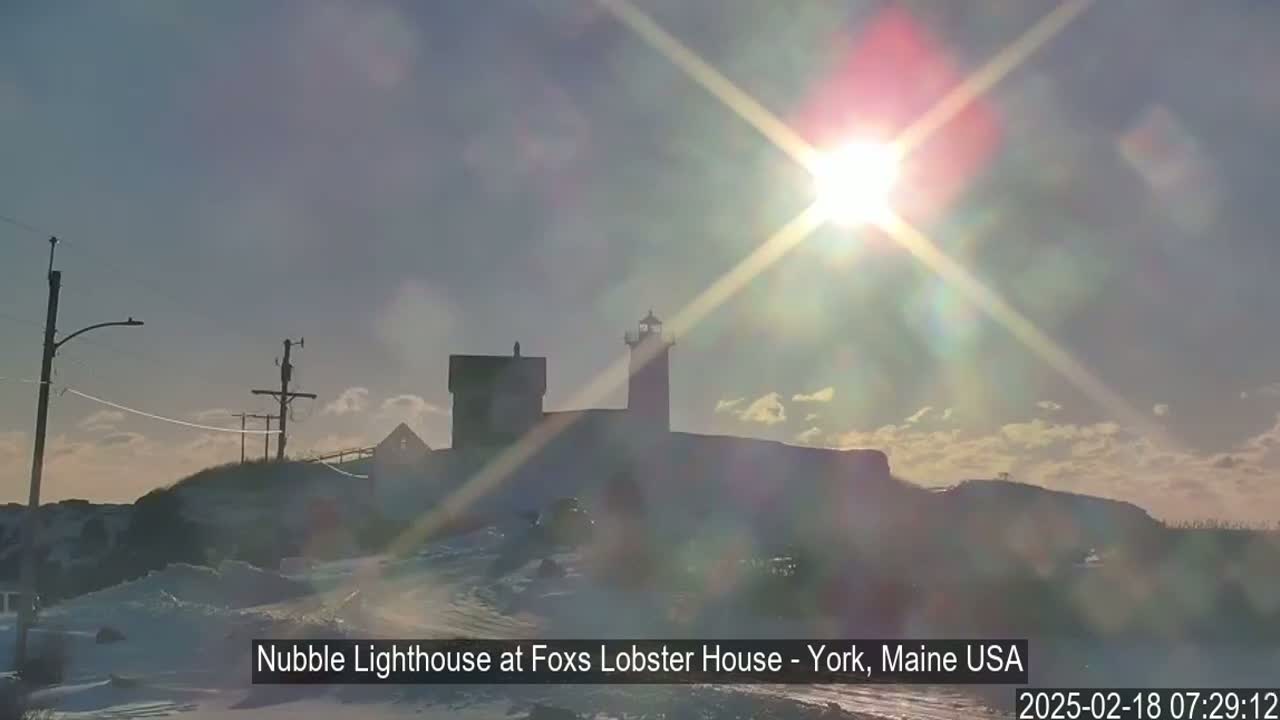 A snow-covered landscape features a lighthouse silhouetted against a bright, sunny sky.