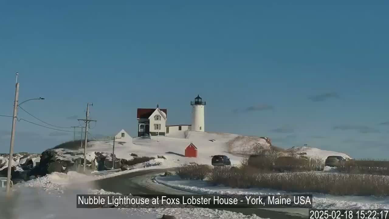 A snow-covered landscape features a lighthouse and nearby buildings, with a clear blue sky.