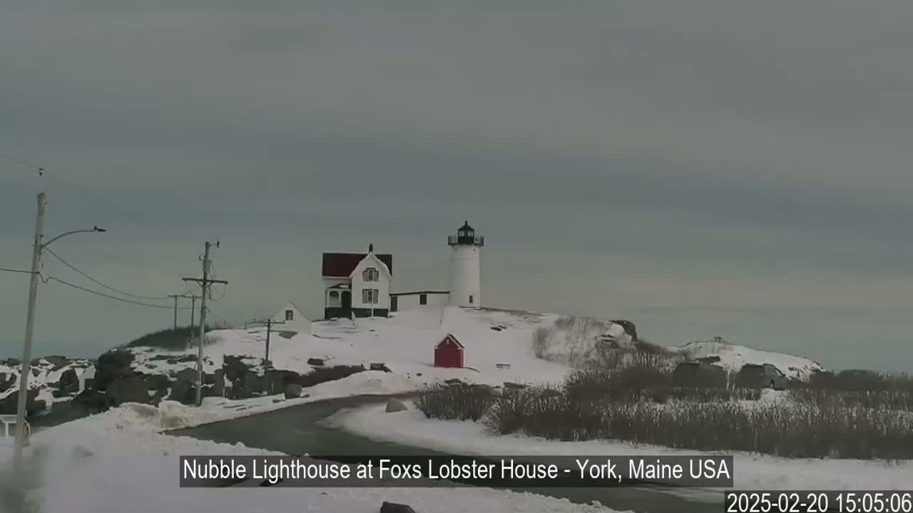 A snow-covered landscape features a lighthouse and accompanying buildings, with a gray overcast sky.