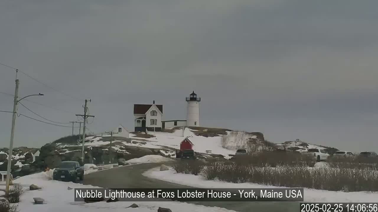 A white lighthouse and a house sit atop a snow-covered hill on an overcast day.