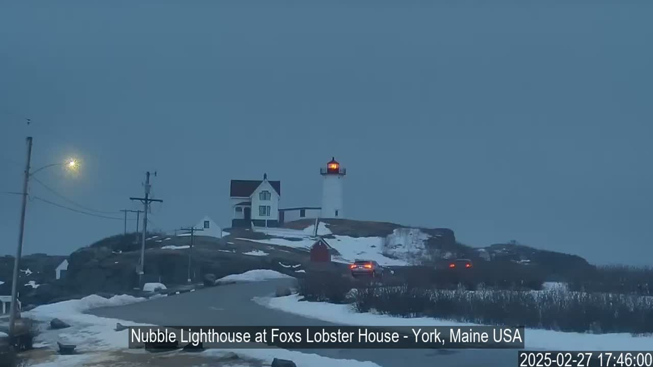 A lighthouse stands on a snow-covered rocky hill under a gray, overcast sky.