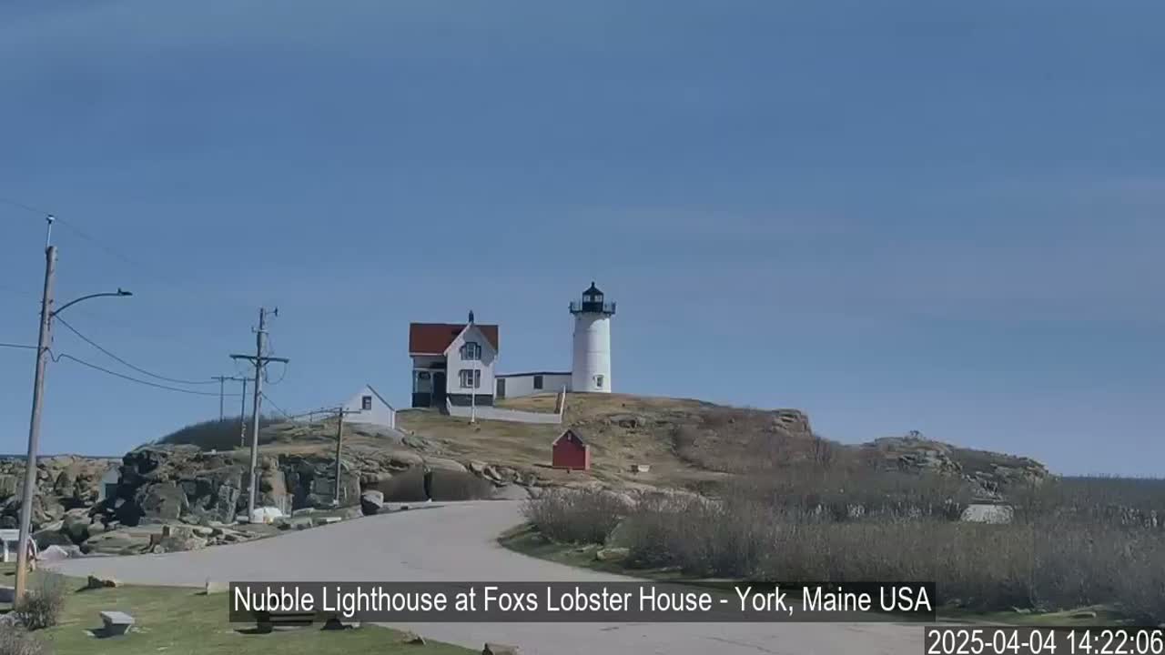 A white lighthouse and adjacent buildings sit atop a rocky hill under a clear blue sky.