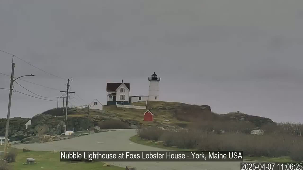 A lighthouse and keeper's house sit atop a rocky hill under an overcast sky.