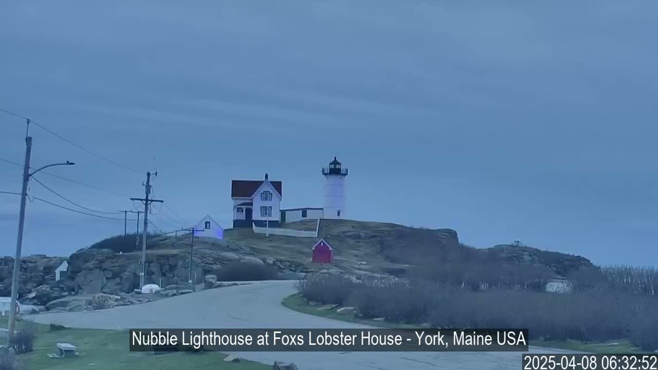 A lighthouse and accompanying building sit atop a rocky outcropping under a cloudy, overcast sky.