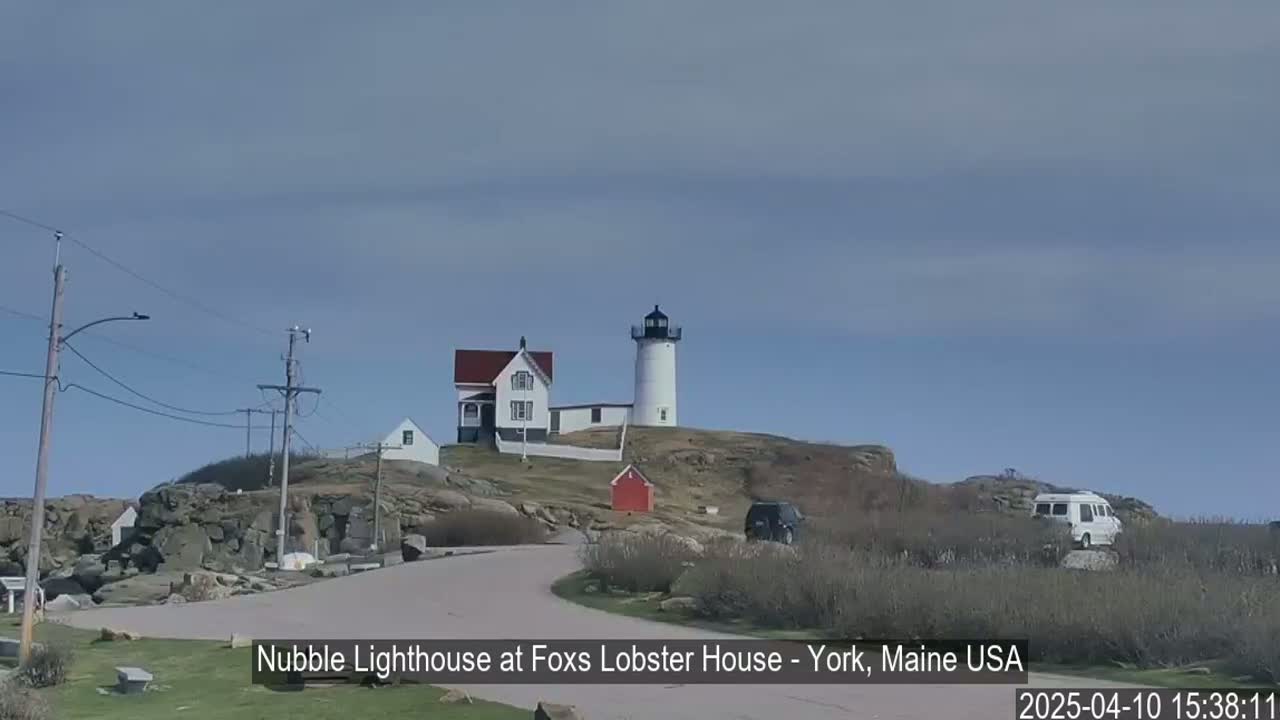 A lighthouse and keeper's house sit atop a rocky hill under a mostly clear sky.