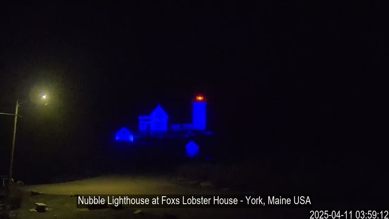 A lighthouse and nearby buildings are illuminated in blue at night.