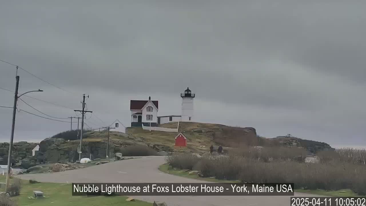A white lighthouse and keeper's house sit atop a rocky outcrop on an overcast day.