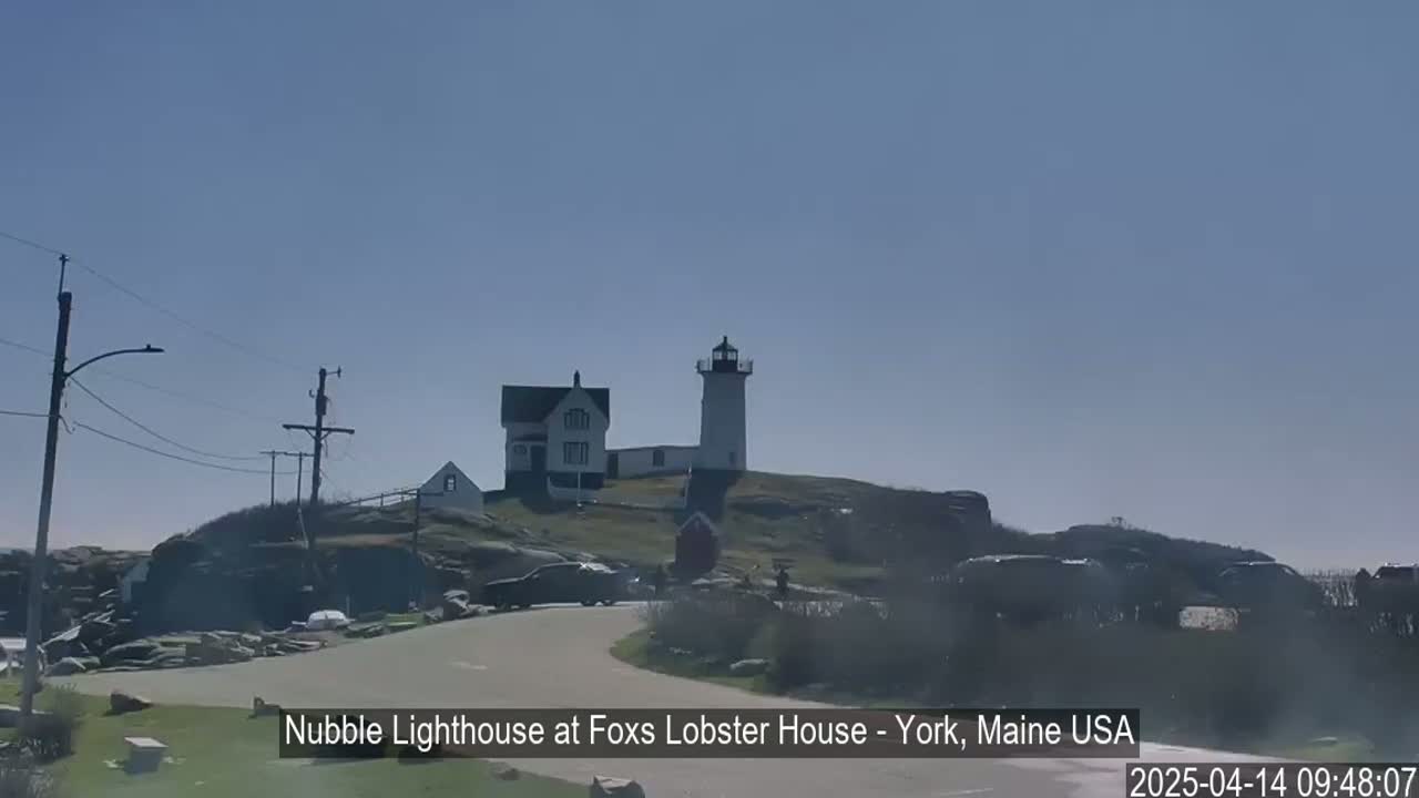 A lighthouse and accompanying buildings sit atop a rocky hill on a clear, sunny day.