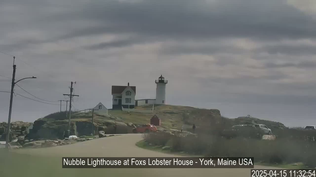 A white lighthouse and a smaller house sit atop a rocky hill under an overcast sky.